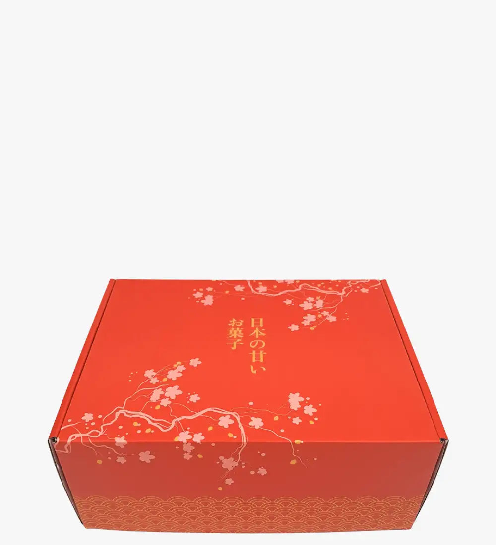 Röd kartonggåvobox med delikat vita körsbärsblomsmönster och guldbladsmönster, med japansk text längs sidan.