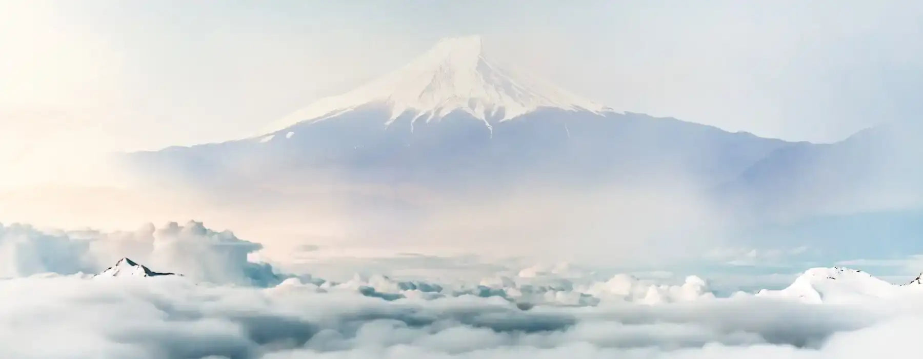 Snötäckta berget Fuji reser sig majestätiskt över ett hav av fluffiga vita moln under en mjuk, dimmig himmel.
